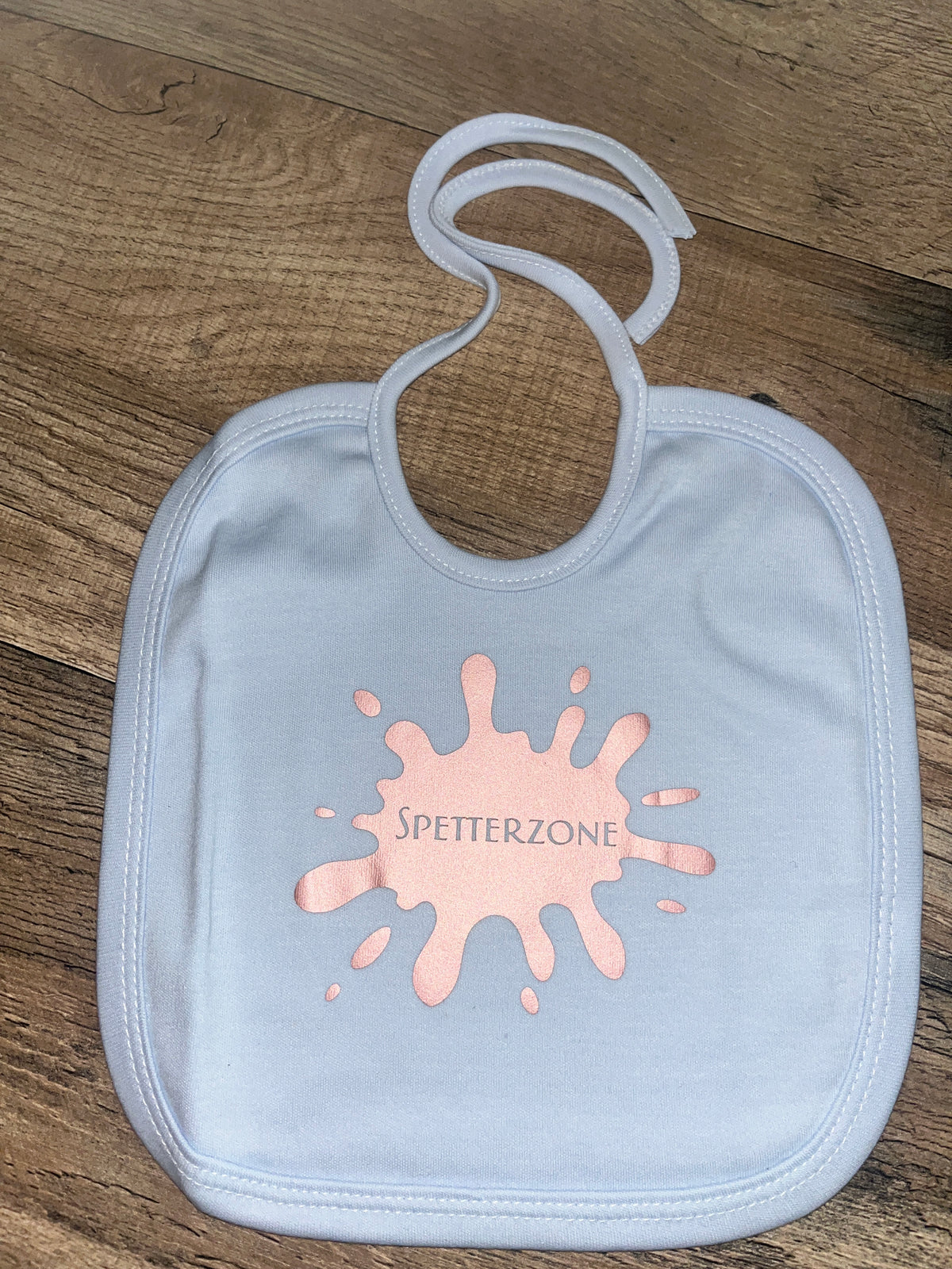 Lichtblauw babyslabbetje met lichtroze spatvorm en tekst Spetterzone