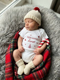 Baby draagt wit rompertje met bordeauxrode opdruk Mijn eerste Kerst, sterren en kerstboompje