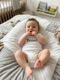 Baby draagt witte romper met korte mouwen en tekst Broer.