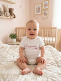 Baby draagt witte romper met korte mouwen en Poppemie-opdruk